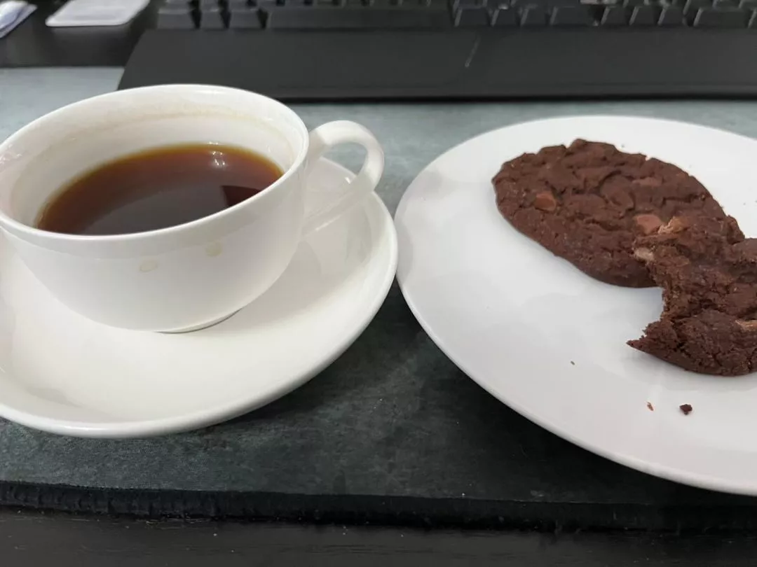 An image showing black coffee and a half eaten chocolate cookie