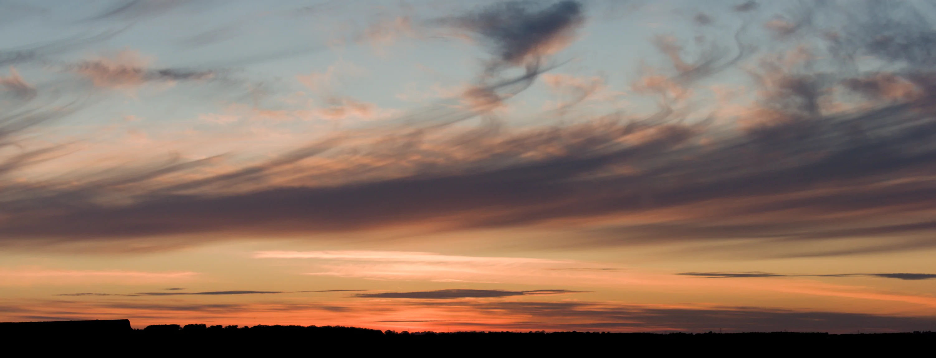 A soft orange sunset, behind a sky of light whispy clouds